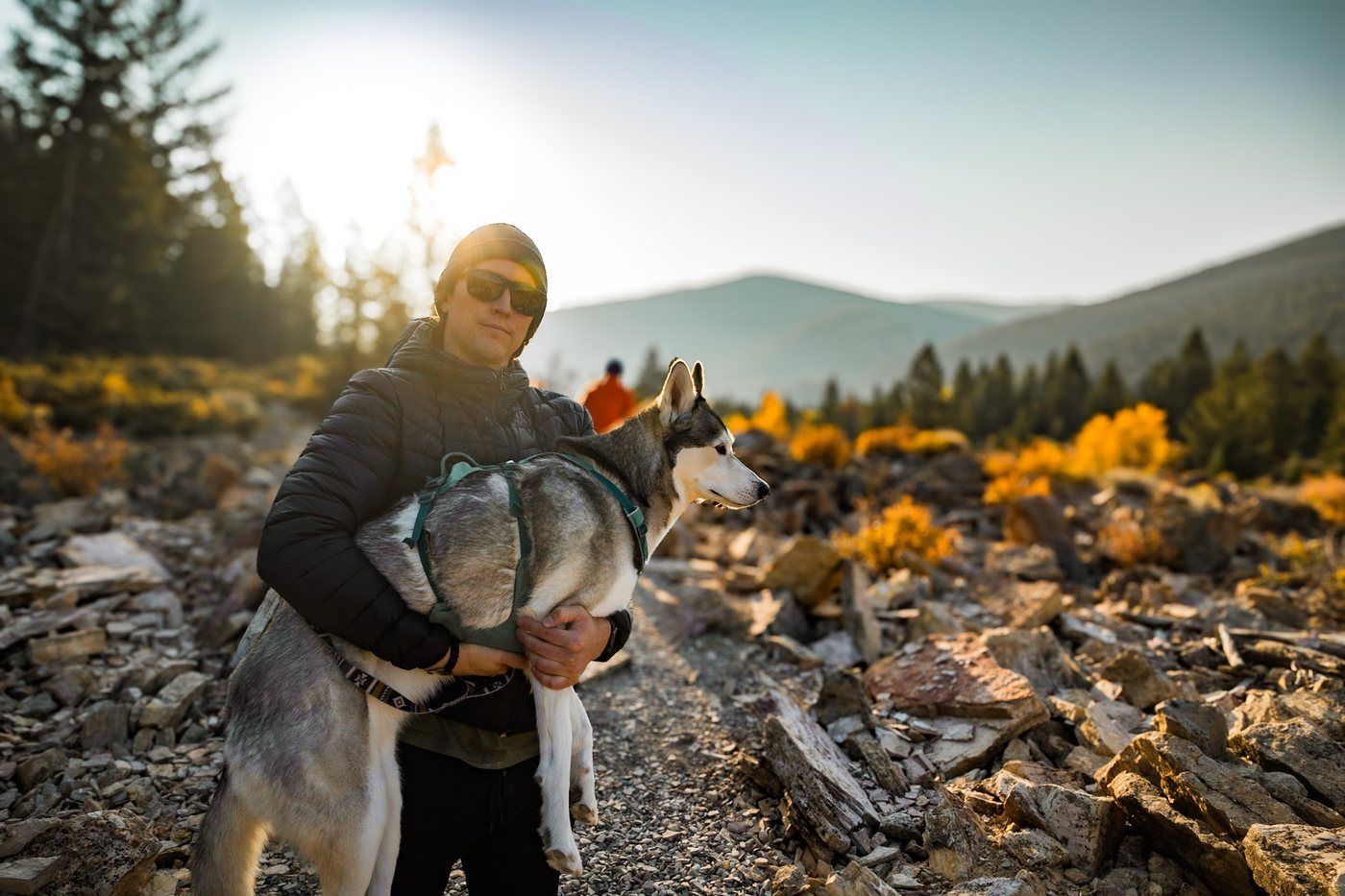 Holding my husky on a rocky trail at sunrise, fall colors behind us