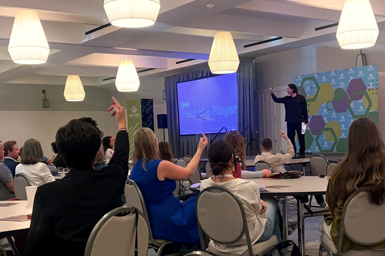 Jonathan Smithgall on stage at OneWest, the audience with hands raised